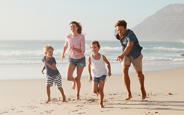 mor, far, to barn løper på en strand på ferie, reise